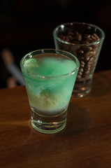 high angle view of shot glass with blue alcohol drink near glass with coffee beans on wooden table in bar