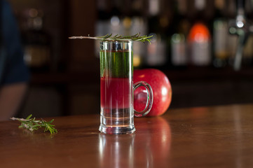 selective focus of shot glass with multicolored alcohol drink and rosemary on near red apple on...