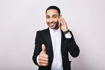 Stylish portrait young handsome man in white shirt, black jacket smiling to camera, talking on phone on white background. Success, great work, meeting, smiling, expressing true positive emotions