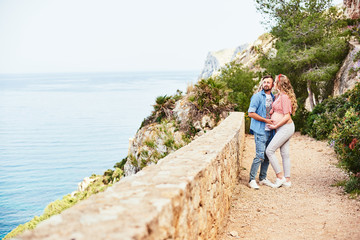 Young pregnant woman posing with her husband against sea background