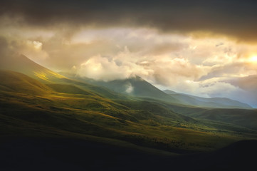 Low evening sunlight at dusk illuminates the hilly green hillsides and low clouds. Nature of the North Caucasus