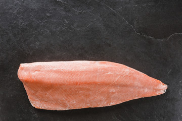 Frozen salmon fish fillet steak on dark stone background. Seafood, top view, flat lay