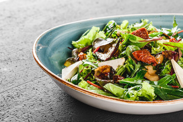 Healthy salad with grilled eggplant, greens, arugula, spinach, lettuce, dried tomatoes and cheese in plate over dark table. Healthy vegan food, clean eating, dieting.