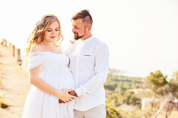 Obraz premium Portrait of a young pregnant woman posing with her husband on a sunny summer day