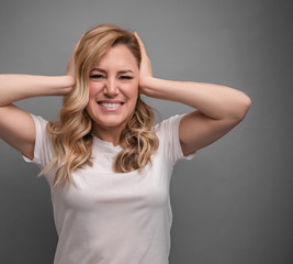 Fototapeta premium Attractive woman covers her ears with hands on a gray background.