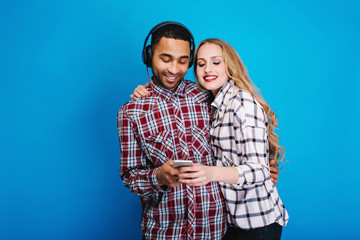 Happy moments of joyful couple listening to music on blue background. Having fun, using phone, hobby, weekends, free time, enjoying songs, expressing positivity, smiling, lovers