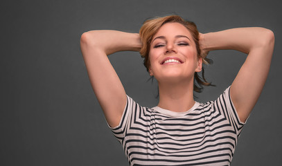 Young woman relaxing with hands behind head on gray background.