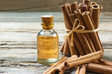 Close up bottle of cinnamon oil with cinnamon sticks on wooden background,  healthy spice concept