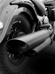 monochrome close up of the back of a vintage motorcycle with rear wheel mudguard and wide exhaust...
