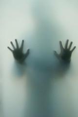 Ghostly silhouette of a girl with outstretched hands, fingers outstretched behind the translucent glass doorBlurred shadow of a horror woman. 