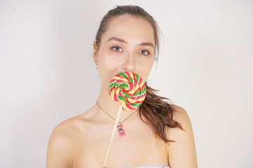 cute feminine caucasian girl stands in a transparent thin summer shirt with a round colorful candy in her hand on a white background in the Studio