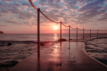 Sunrise at Bronte Beach Pool, New South Wales, Australia. Waves on the rocks.
