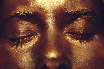 Macro of dark gold young girl face . Bright tanned and shiny sexy woman bronze skin sparkles at...