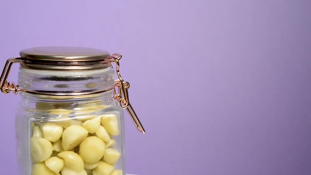Close up of an airtight mason jar rotating with macadamia nuts on a neon lilac background. Flat plane. Eye level