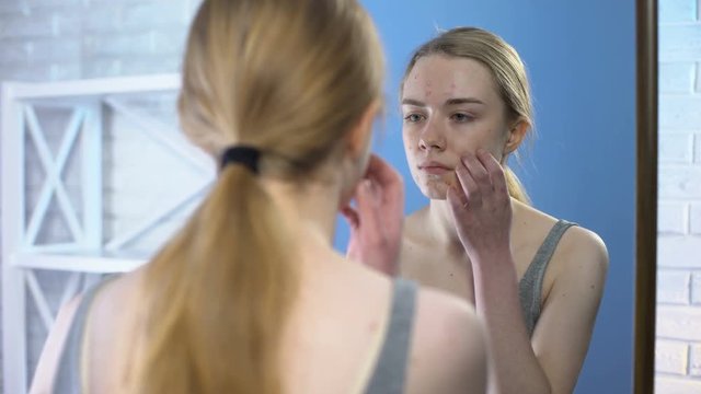 Teenage female with face pimples looking mirror, puberty skin problem, hormones