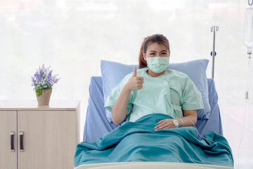 Asian patient  sitting on hospital bed with hand gesture thumbs-up. The young woman recover from illness. Healthcare and medical concept.
