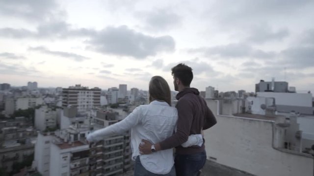 Wide shot of young couple stretching their hands while looking at cityscape during dusk