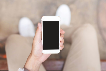 Close up of a young man hand holding using mobile smart phone with screen empty cell phone. he sitting chair in public park outdoor. Top view with copy space.