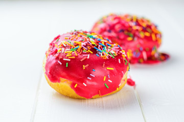 Two red pechnika in colorful topping on a white wooden table.