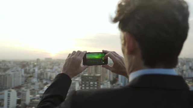 Medium shot of mature businessman taking picture of city with smartphone during sunset