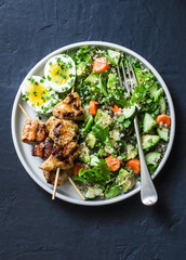 Healthy balanced lunch bowl - turkey skewers, quinoa, avocado, cucumber salad and boiled egg on dark background, top view. Mediterranean style food