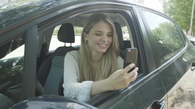 Medium shot of young woman taking photograph with smartphone while sitting in car