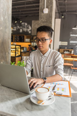 Fototapeta premium Young Asian freelancer working on laptop at cafe
