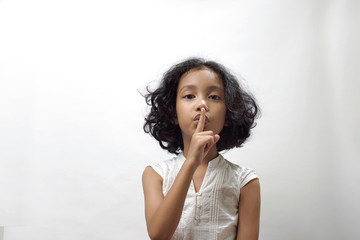 A girl shows an expression telling her not to be noisy, by holding her index finger to her lips.