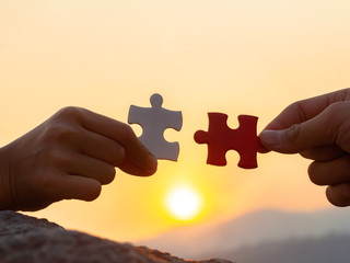 hands holding piece of jigsaw puzzle at sunset background. teamwork concept