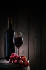 Fotobehang Red wine in glass and bottle standing on barrel with bunch of grapes © alexlukin
