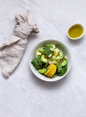 fresh vegan salad bowl with avocado, spinach, corn, chickpeas, zucchini on marble background with copy space