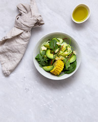 fresh vegan salad bowl with avocado, spinach, corn, chickpeas, zucchini on marble background with copy space