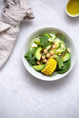 fresh vegan salad bowl with avocado, spinach, corn, chickpeas, zucchini on marble background with copy space