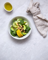fresh vegan salad bowl with avocado, spinach, corn, chickpeas, zucchini on marble background with copy space