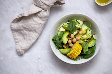 fresh vegan salad bowl with avocado, spinach, corn, chickpeas, zucchini on marble background with copy space