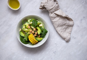 fresh vegan salad bowl with avocado, spinach, corn, chickpeas, zucchini on marble background with copy space