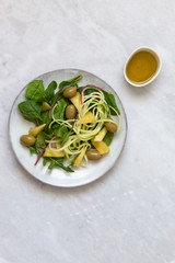 Vegetarian salad with pineapple, olives, tofu, zucchini, spinach and chickpeas in rustic plate on marble background with copy space