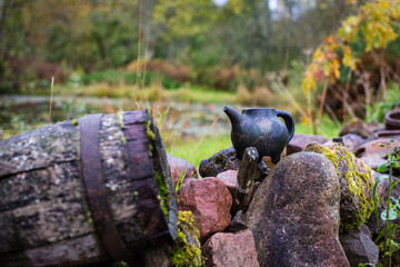 Black clay jug and old wooden barrel on stone pile.