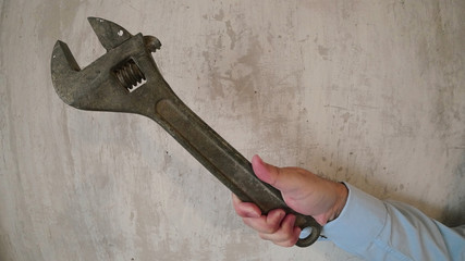  A male hand in an office shirt holds a large adjustable wrench over the hem and guides them. Background old concrete wall.  