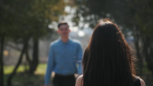 Young boy came to his girlfriend, kiss her and showed a camera behing her. Young positive couple in the park.