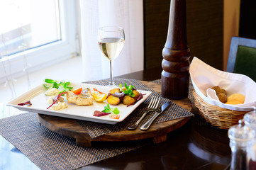 A piece of fish with vegetables and fried potatoes on a plate