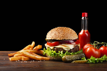 Homemade hamburger close-up with beef, tomato, lettuce, cheese, french fries sauce bottle on wooden table. Fastfood on dark background