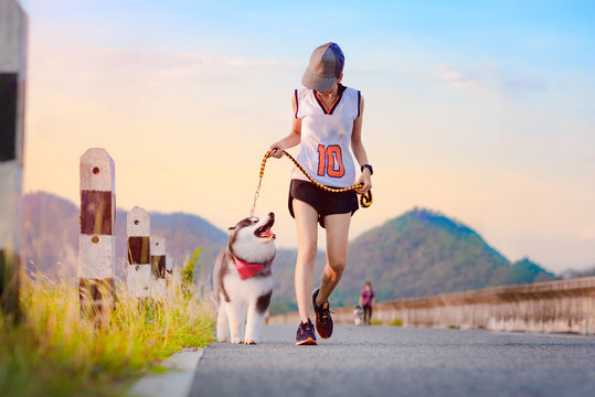 Woman doing daily exercise jogging on the public park road with puppy breed dog