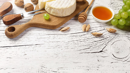 White wine bottle, grape, honey, cheese and wineglass on white wooden board