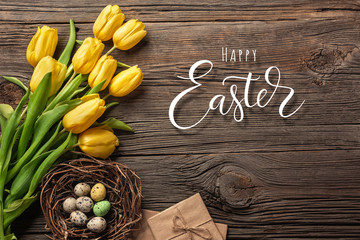 Easter background with colorful eggs and yellow tulips on wooden table. Top view