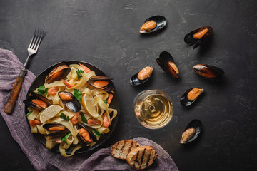 Spaghetti vongole, Italian seafood pasta with clams and mussels, in plate with herbs and glass of white wine on rustic stone background. Traditional Italian sea cuisine, close-up, top view