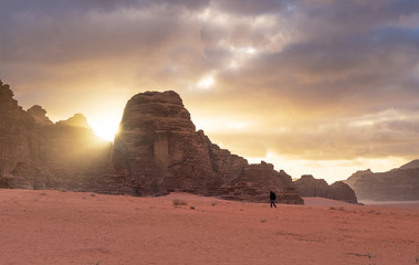 Fototapeta na wymiar Landscape of Wadi Rum desert in sunrise with a man walking alone, and sunlight through stone mountain. Travelling and adventurous in desert, Jordan