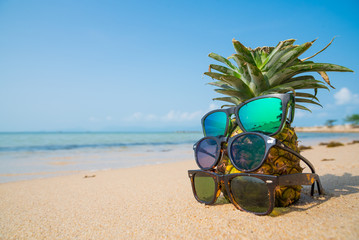 Pineapple with sunglasses on tropical beach background. Summer concept