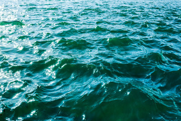 sea ripples; turquoise clear water with small waves close up; sun glare on the water