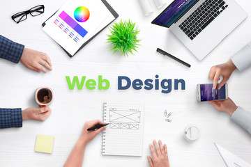 Web design text on work desk surrounded with web development team, devices, projects, and ideas on...